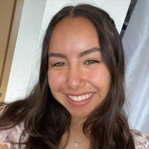 Headshot of Emily Hurtado, who has long straight brown hair and wears a pink top.