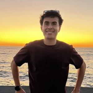 Headshot of Josh Becerra, who has wavy dark hair and wears a black T-shirt.