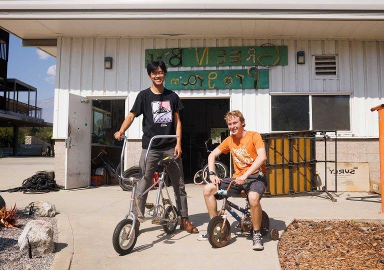 two students sit on mini bikes outside the green bike program building